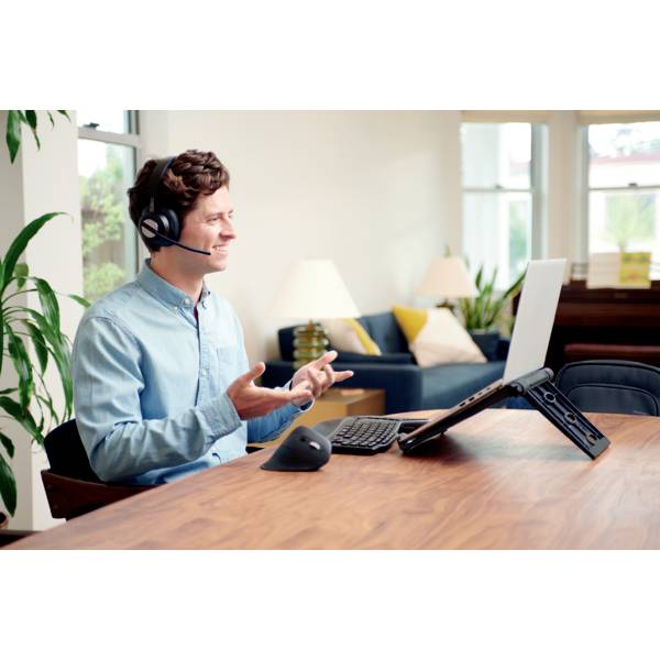 Un homme portant un casque est assis à une table avec un ordinateur portable, sourit et fait des gestes comme s'il participait à une réunion virtuelle.