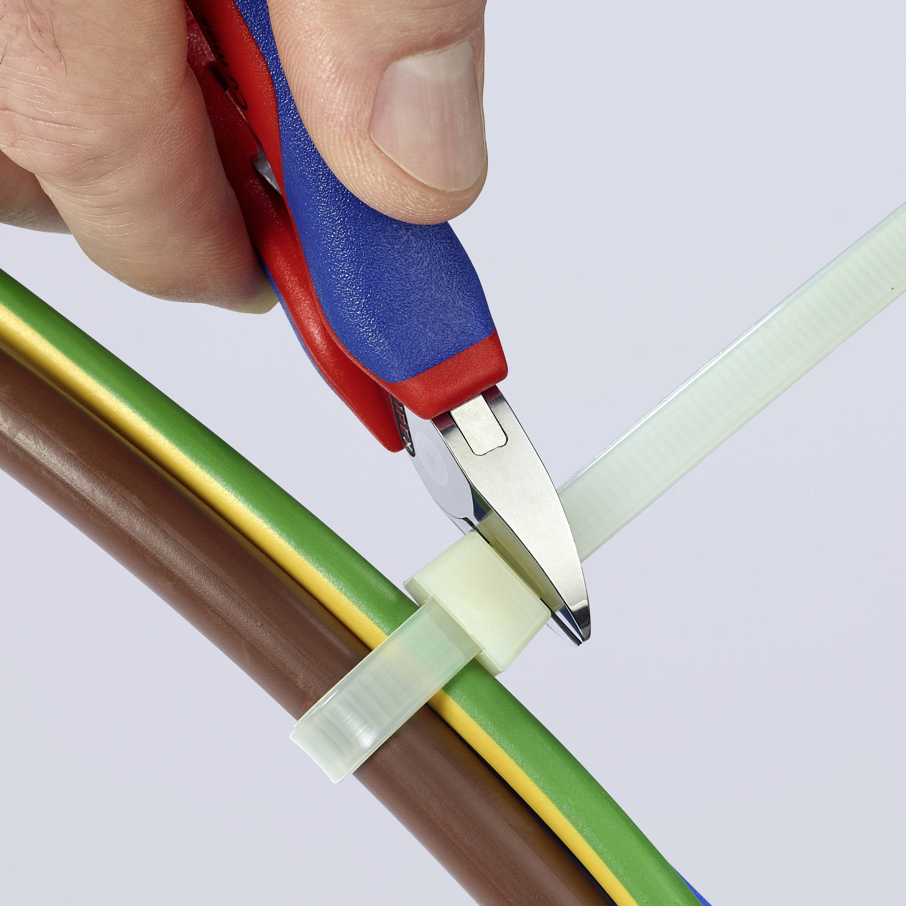 Une main tient un coupe-câble et coupe un collier de serrage qui maintient plusieurs câbles colorés.