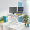Un bureau réglable en hauteur avec moniteur, ordinateur portable, clavier et plantes. Aménagement de bureau lumineux et moderne à l'esthétique minimaliste.