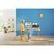 Une femme est assise à un bureau avec deux écrans montrant des sites web. Un espace moderne et coloré avec un tabouret jaune et un mur bleu.