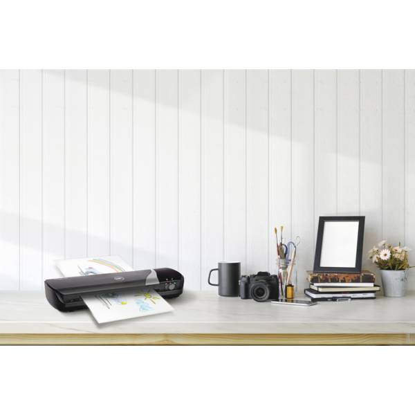 Imprimante sur un bureau en bois délivrant une page en couleur ; à côté, une tasse, un appareil photo, des carnets, un cadre photo et un vase avec des fleurs.