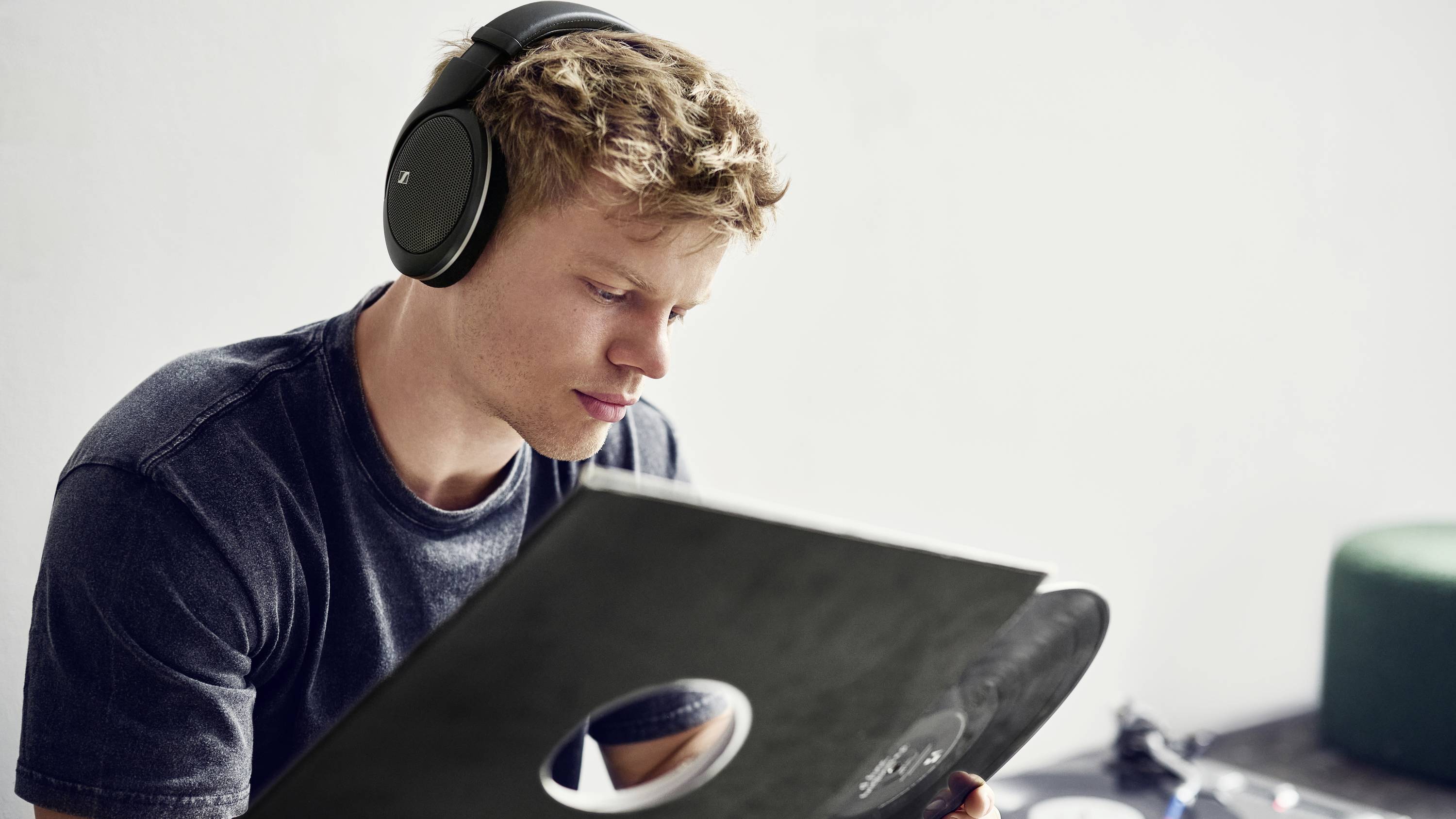 Un homme est assis avec des écouteurs et examine un disque vinyle. La pièce est aménagée de manière minimaliste.