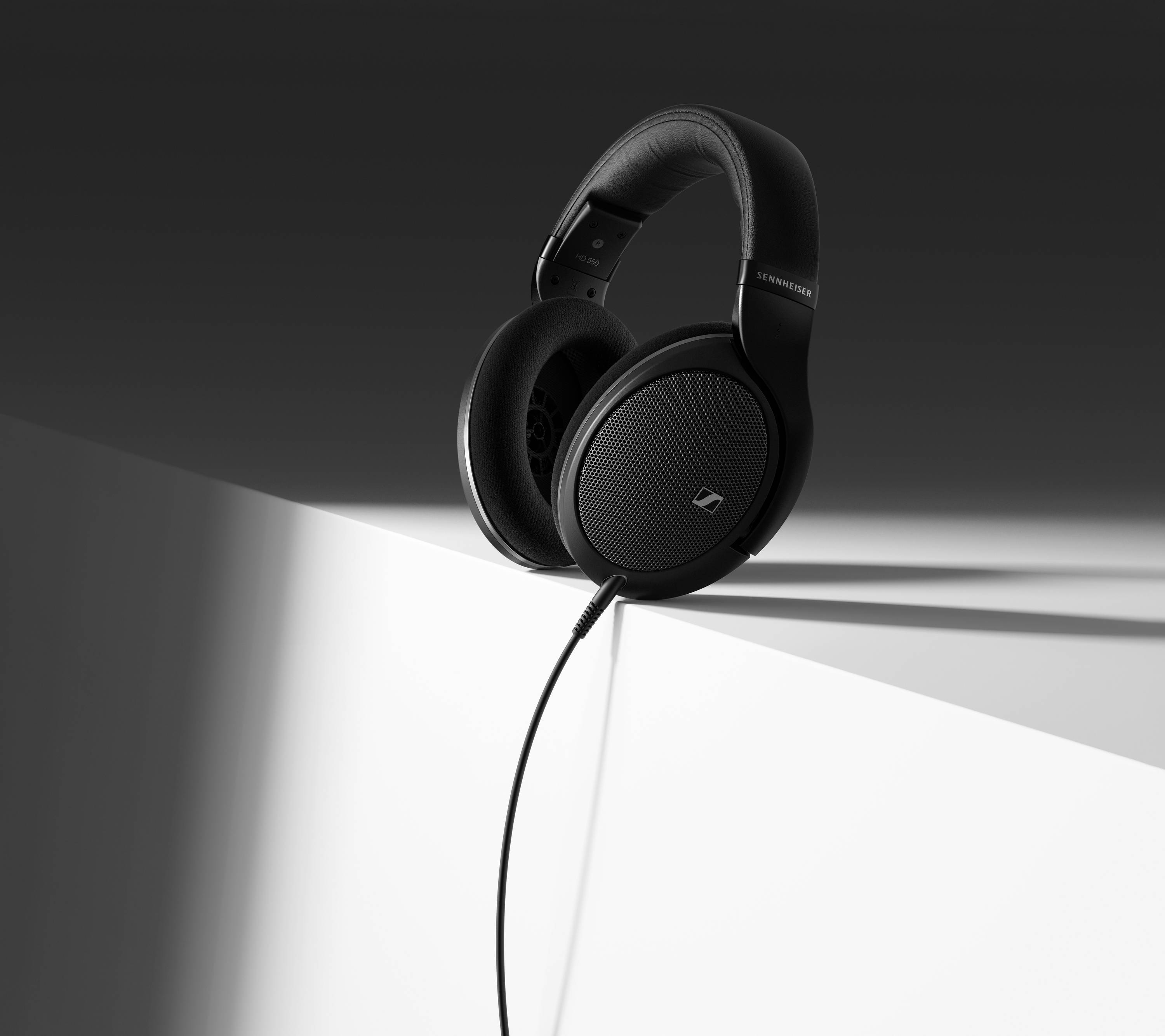 Un casque noir à écouteurs circumauraux est posé sur une surface blanche inclinée. Le câble pend de manière décontractée. L'arrière-plan est gris foncé.