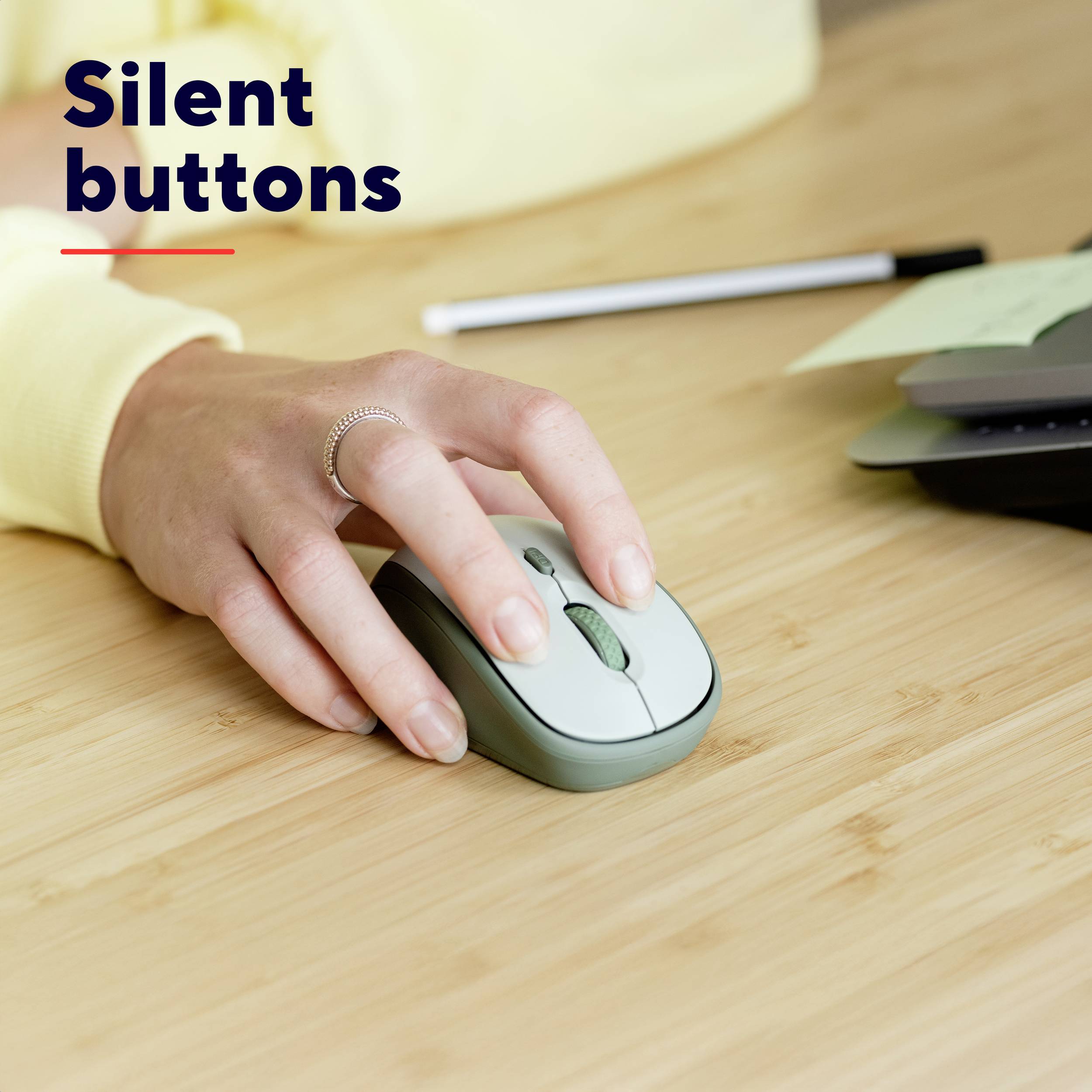 Une personne utilise une souris sans fil silencieuse sur une table en bois. À côté se trouvent un stylo et un carnet de notes. Texte : 'Silent buttons'.