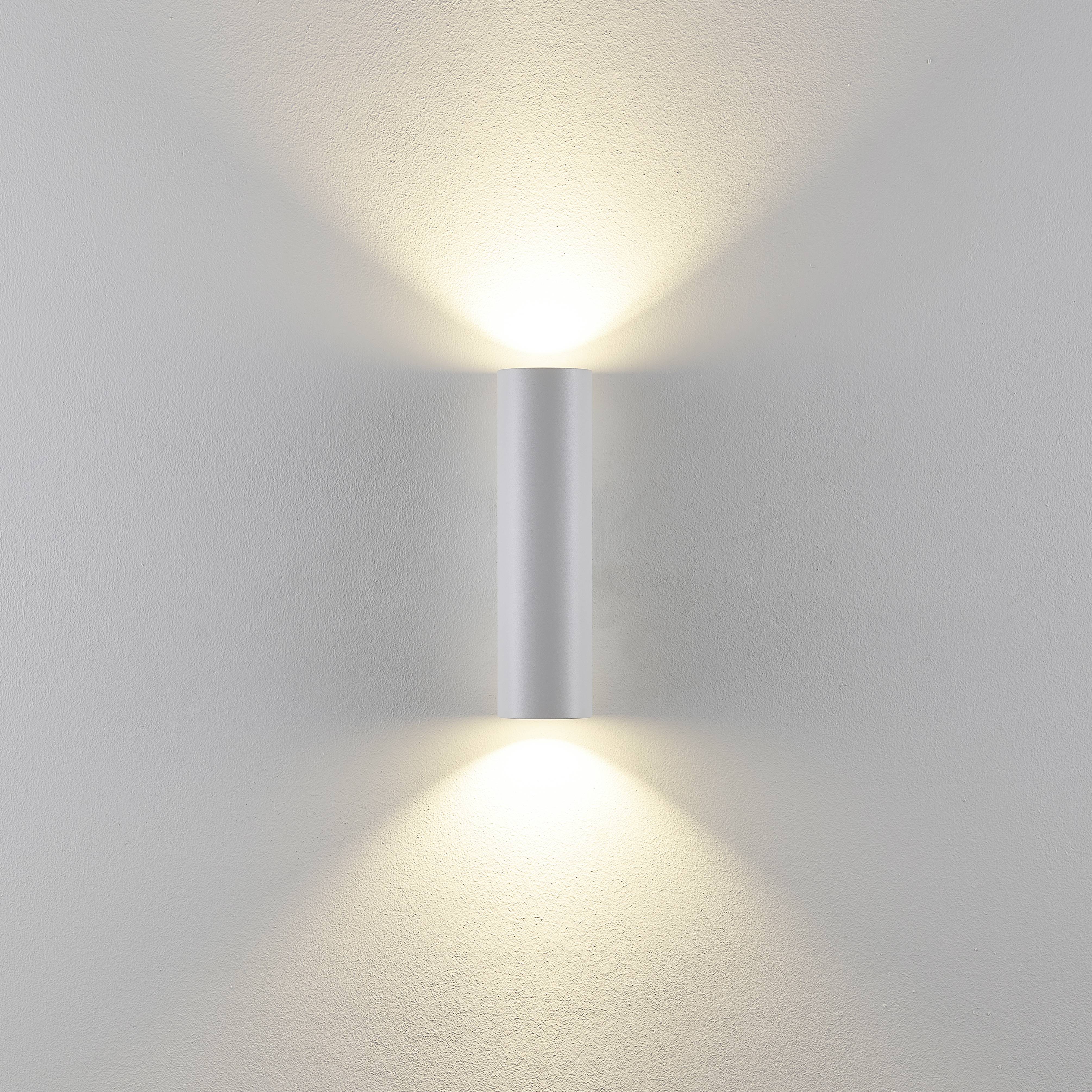 Lampe murale cylindrique blanche projetant de la lumière vers le haut et vers le bas, créant des effets lumineux doux sur le Mur.