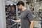 Un homme portant un t-shirt gris fait fonctionner une machine dans un hall d'usine tout en regardant un appareil portable.