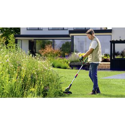 Une personne tond la pelouse avec un coupe-bordures devant une maison moderne. En arrière-plan, on aperçoit un pré fleuri luxuriant.