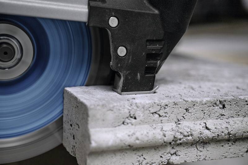 Gros plan d'une scie circulaire en train de couper du béton. La lame bleue tourne à grande vitesse et génère de la poussière de béton.