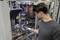 Un homme portant des lunettes de protection et des protections auditives contrôle des tuyaux ou des pièces de machine à l'aide d'un appareil numérique dans un hall d'usine.