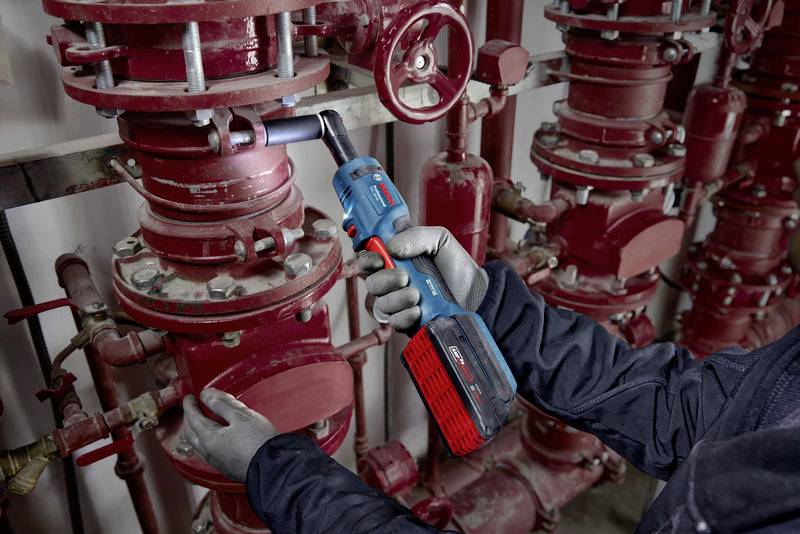 Une personne fixe une vanne rouge à l'aide d'un tournevis sans fil dans une installation industrielle de tuyauterie, entourée de plusieurs tubes.