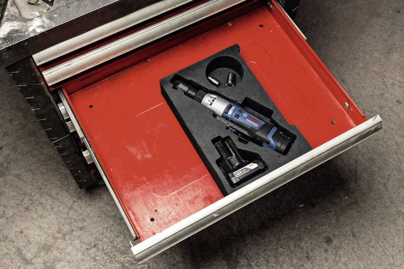 Un tiroir à outils ouvert contient un tournevis électrique avec batterie et station de charge sur un fond rouge.