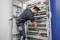 Un technicien travaille sur un armoire électrique, vérifiant les câblages et les connexions. L'armoire contient de nombreux composants électroniques et câbles.