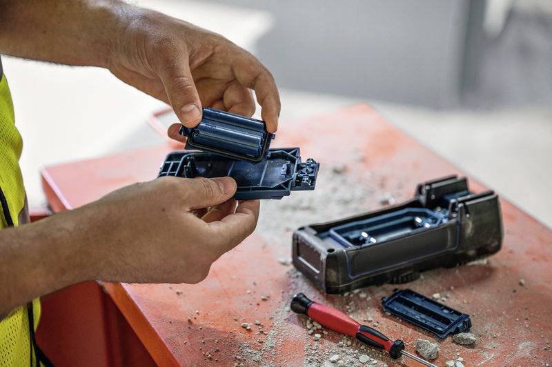 Une personne répare ou inspecte une batterie électrique sur une table avec un tournevis et des débris.