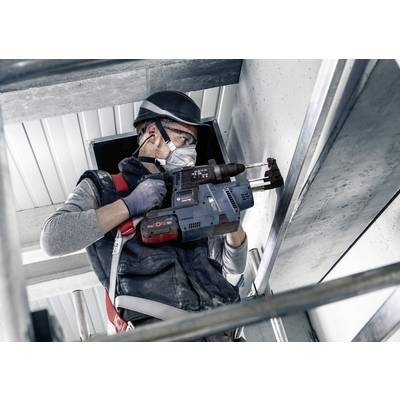 Un ouvrier porte un équipement de protection et utilise une perceuse pour travailler sur une surface en béton. Il se trouve sur un échafaudage.