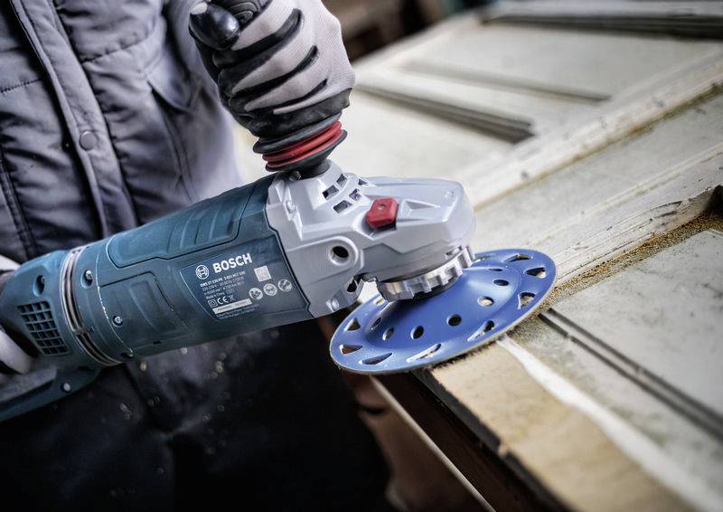 Une personne utilise un outil de meulage Bosch pour poncer la surface d'une poutre en bois afin de la lisser.