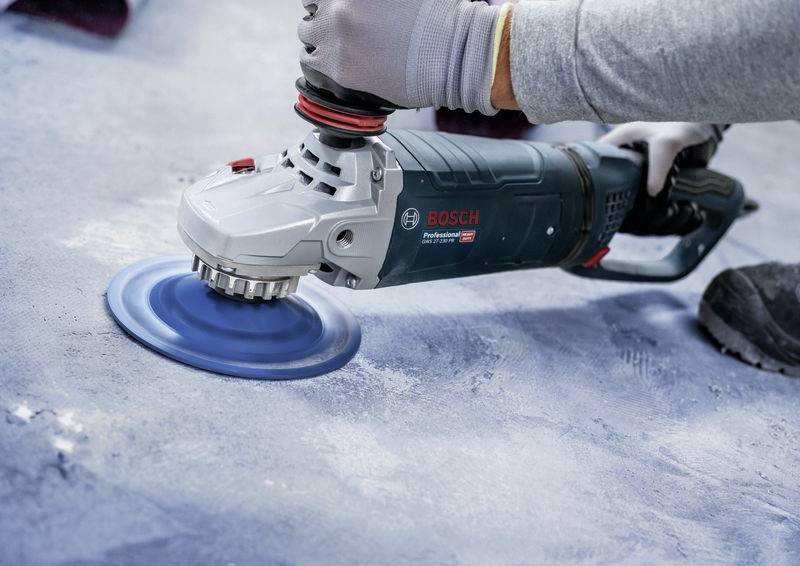 Une personne ponçe une surface à l'aide d'une ponceuse bleue. Un gros plan montre le maniement précis de l'outil pendant le travail.