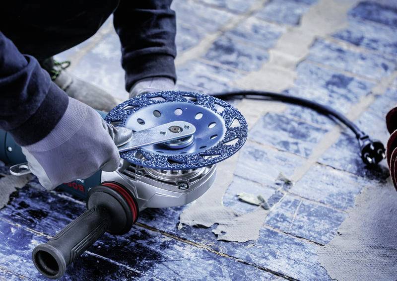 Une personne travaille avec une meuleuse d'angle sur un sol en bois bleu, portant des gants et ajustant le disque de la meuleuse.