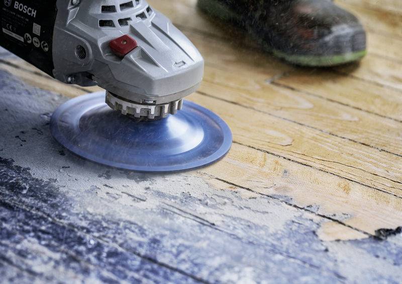 Une personne ponce une surface en bois à l'aide d'une ponceuse électrique pour la lisser. Des copeaux de sciure sont visibles autour de l'outil.