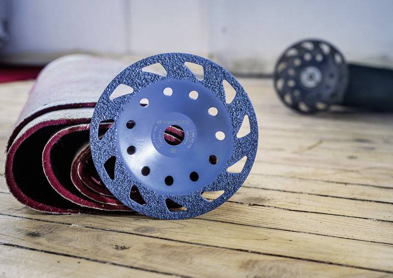 Un disque de ponçage bleu est posé sur un tapis roulé sur un plancher en bois. Un autre disque de ponçage est visible en arrière-plan.