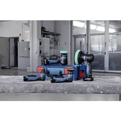 Visseuses sans fil et outils de meulage posés sur un bloc de béton devant un atelier. Noms de marque visibles sur les outils. Environnement moderne.
