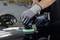 Une personne polit une peinture de voiture avec une polisseuse électrique dans un atelier. Les mains portent des gants gris.