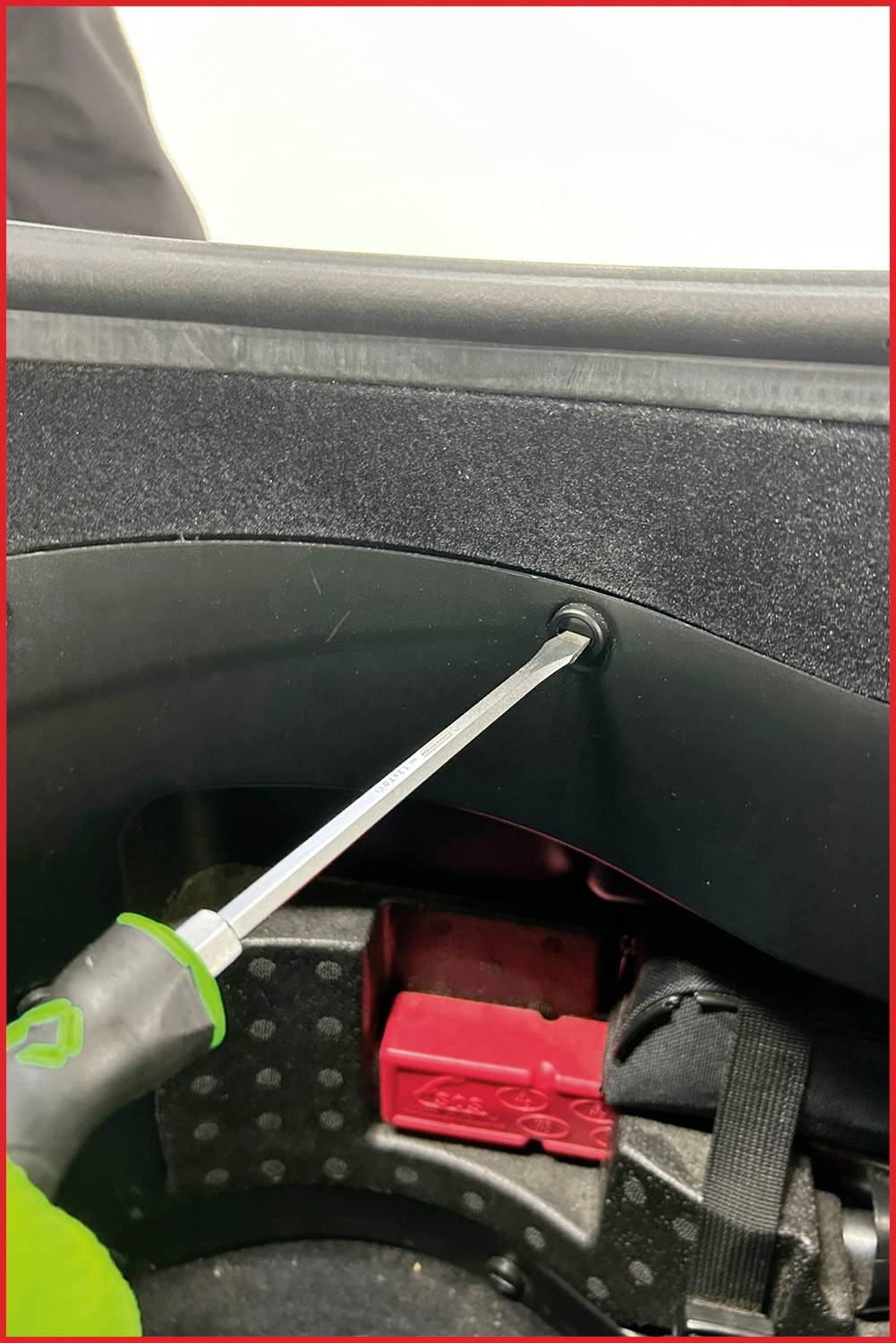 Un tournevis est utilisé pour fixer une vis dans une surface en plastique noir, probablement une partie d'un véhicule.