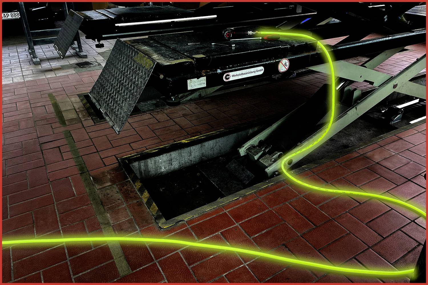 Un atelier automobile avec un pont élévateur. Un câble jaune est éparpillé de manière désordonnée sur le sol, ce qui pourrait représenter un risque de trébuchement.