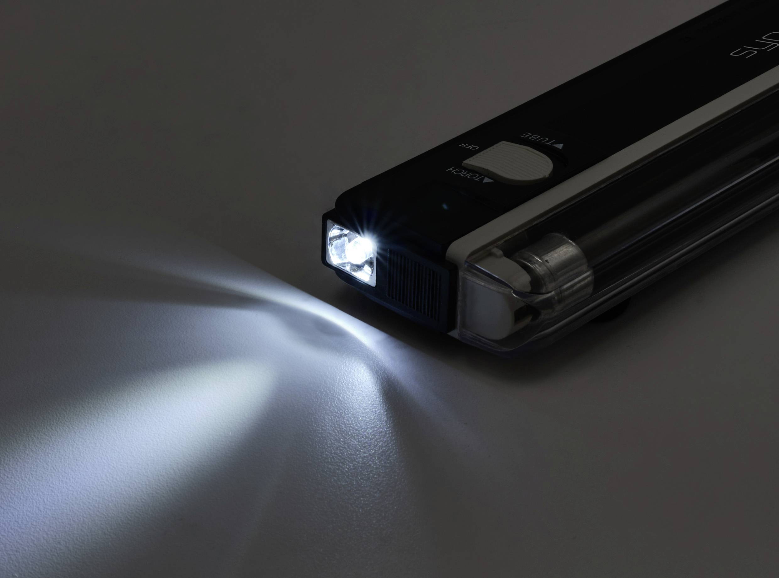 Une lampe de poche compacte posée sur une surface, projetant un faisceau lumineux intense vers la gauche, illuminant une partie de la zone environnante.