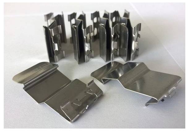 Des trombones de différentes formes et tailles, disposés sur une surface blanche, montrent leur surface métallique réfléchissante.