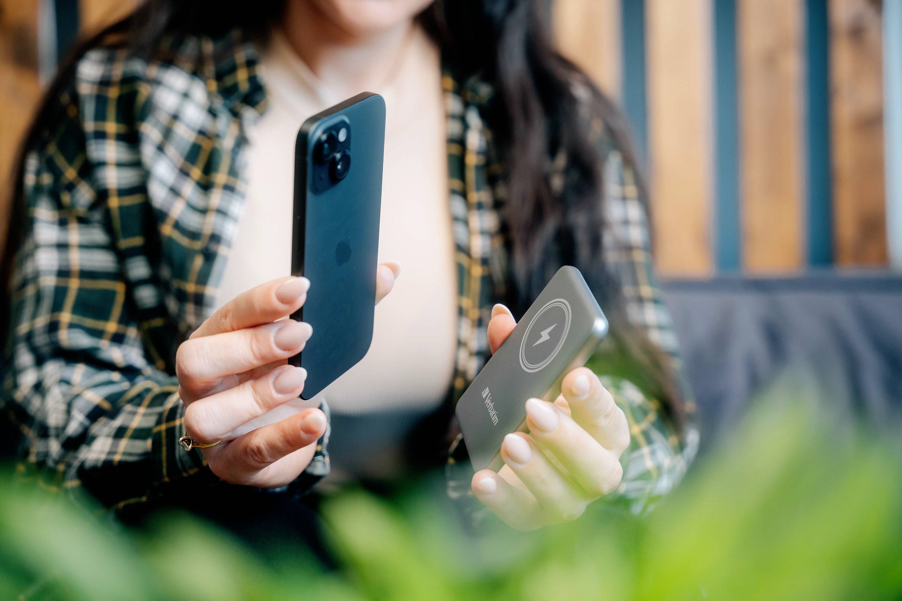 Une femme tient un smartphone dans une main et un chargeur sans fil dans l'autre. Elle semble être en train de charger son téléphone.