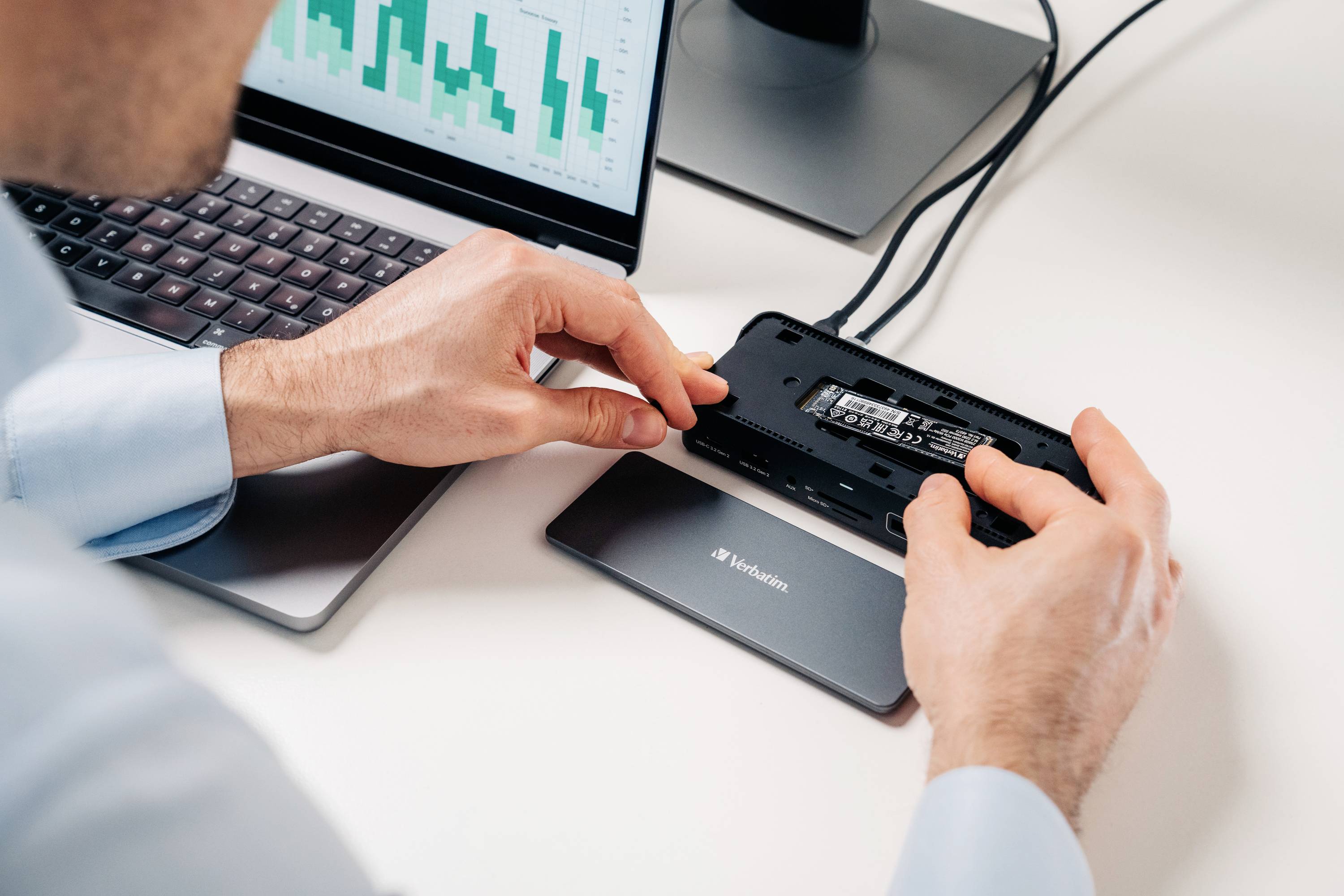 Une personne installe un SSD dans un boîtier de disque externe. Un ordinateur portable affiche des diagrammes. Poste de travail avec technologie.
