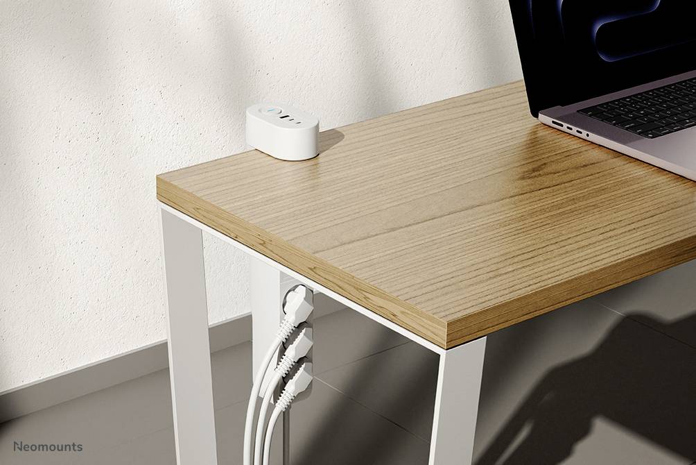 Un bureau blanc avec un plateau en bois, sur lequel les câbles sont soigneusement guidés par un support. Un ordinateur portable est posé sur le bord droit.