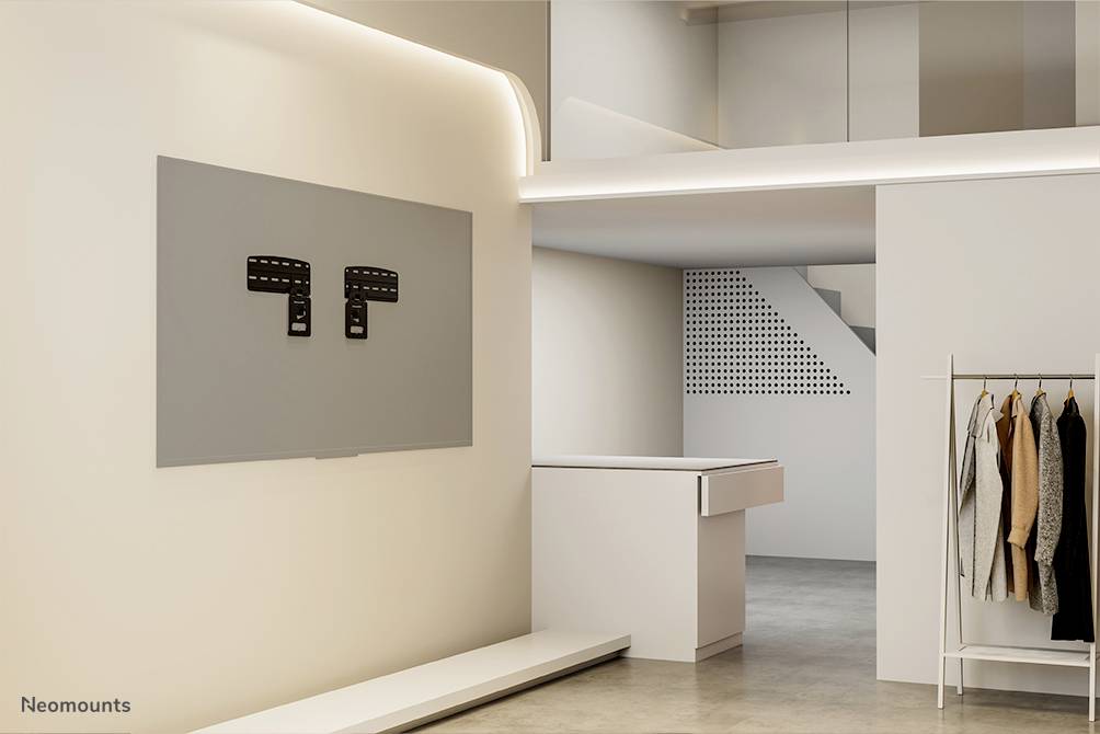 Mur avec support de téléviseur dans un espace de vie moderne et minimaliste. À droite, un portant à vêtements avec des pièces de vêtements, à l'arrière-plan un comptoir d'accueil blanc.