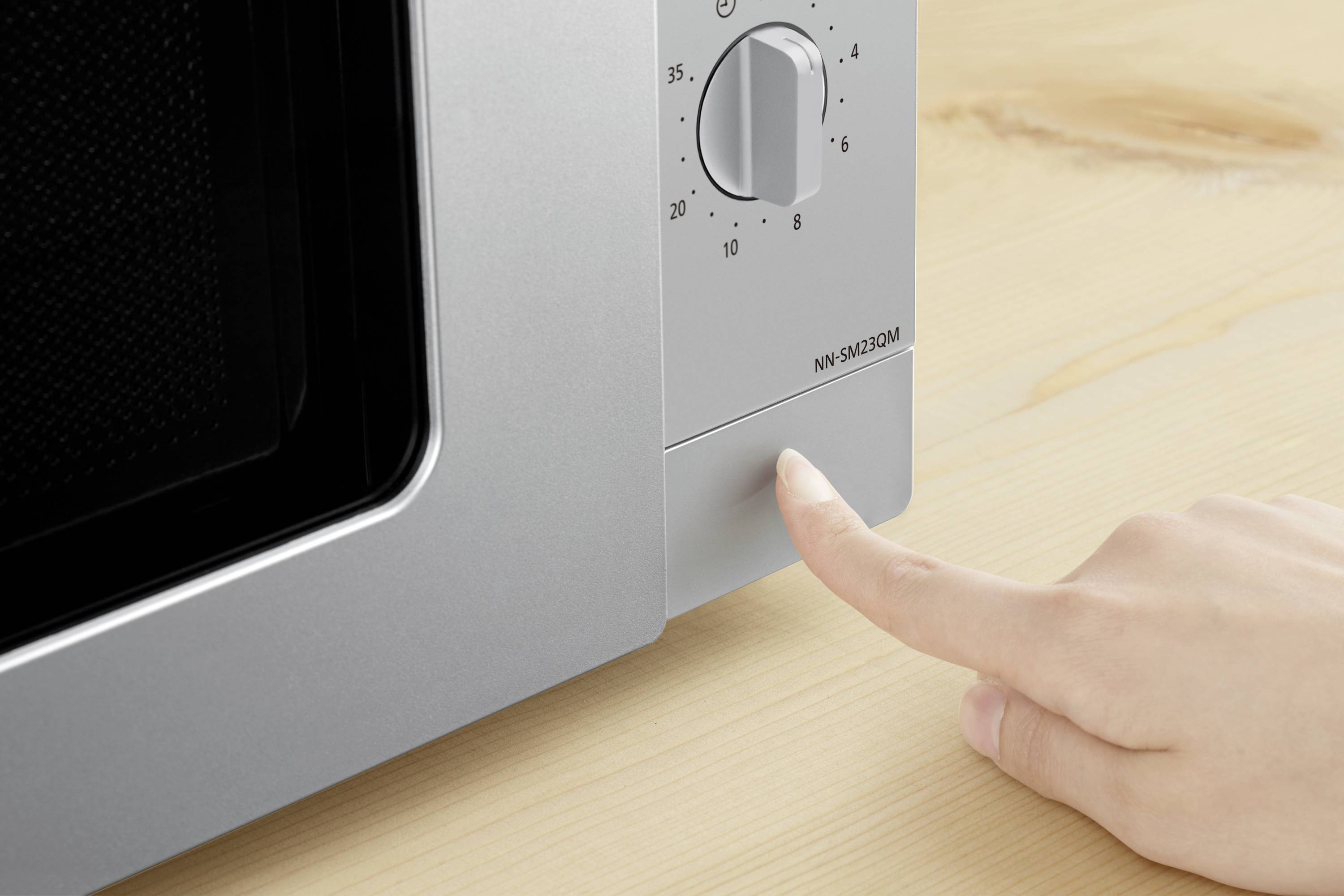 Une main appuie sur la touche d'un four à micro-ondes argenté posé sur une table en bois.