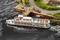 Un modèle de bateau passe devant un port miniature où des figurines sont disposées. Une route et une maison à colombages sont visibles en arrière-plan.