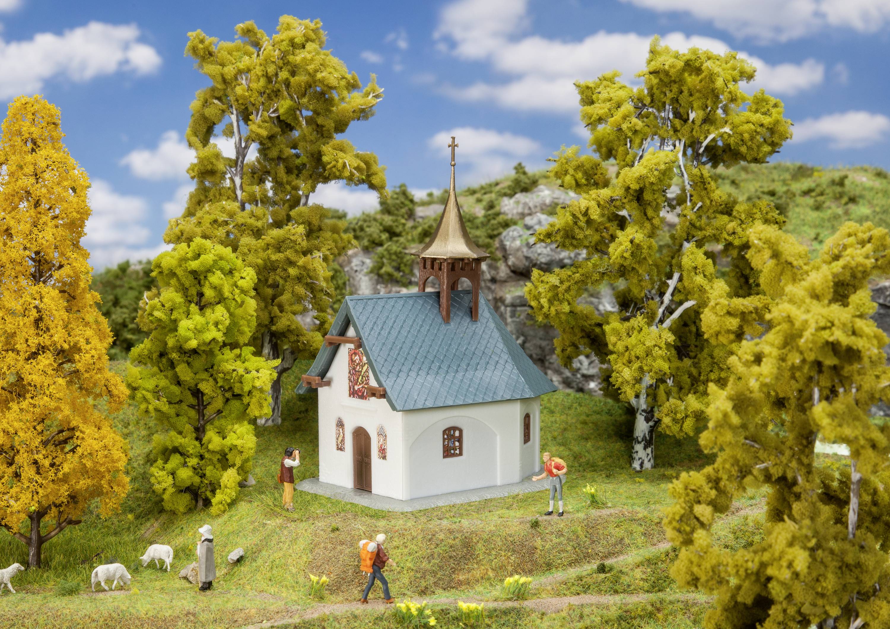 Une petite église dans un paysage rural, entourée d'arbres aux feuilles d'automne. Des personnes et des moutons sont visibles sur un chemin.
