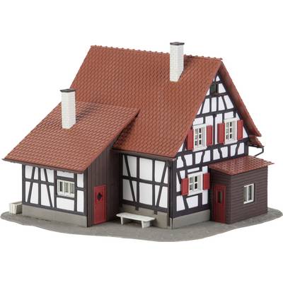 Une maquette d'une maison à colombages avec un toit rouge et deux cheminées. Murs blancs avec des poutres sombres, volets et portes rouges.