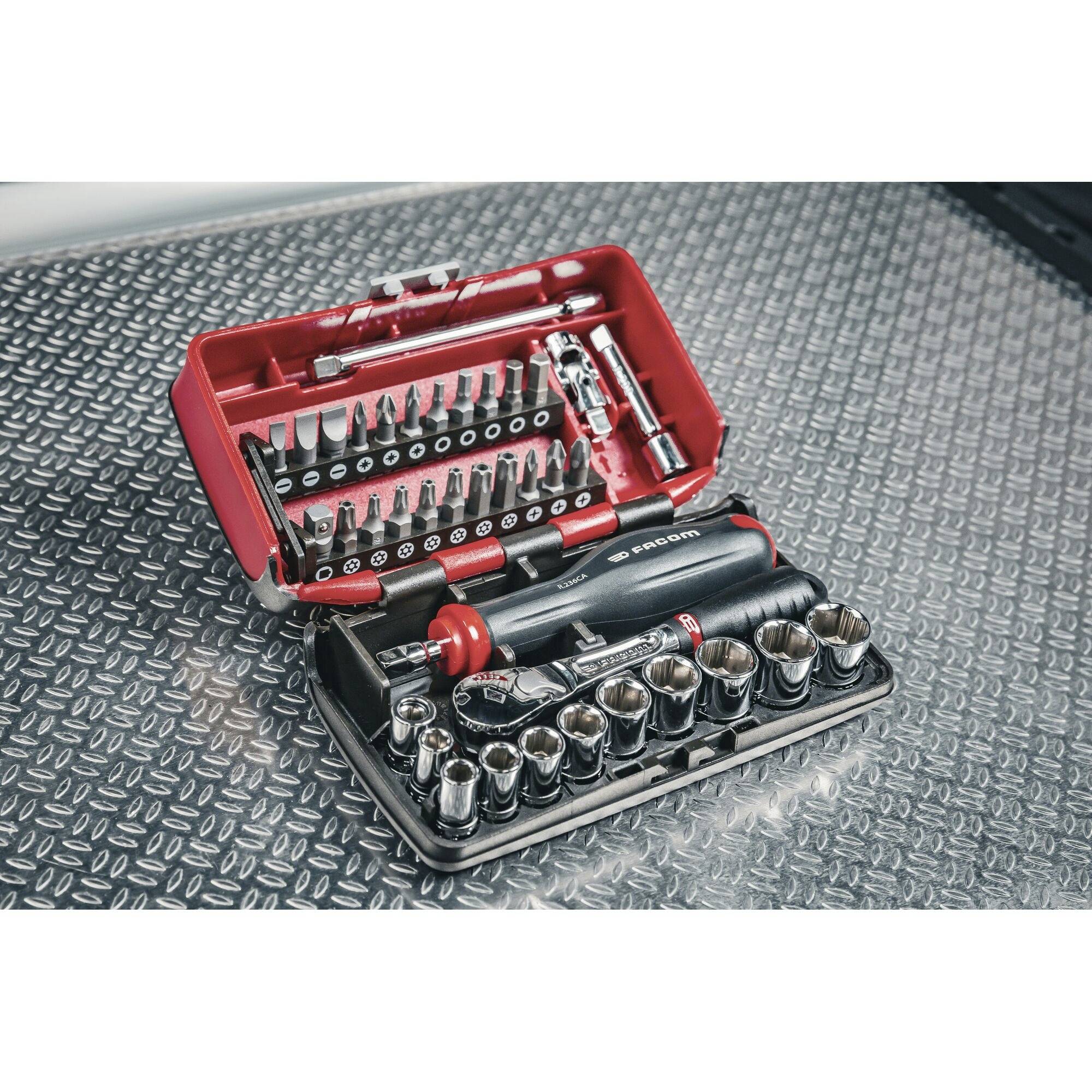 Ensemble de tournevis et de clés à douille dans un coffret rouge ouvert sur une surface métallique.