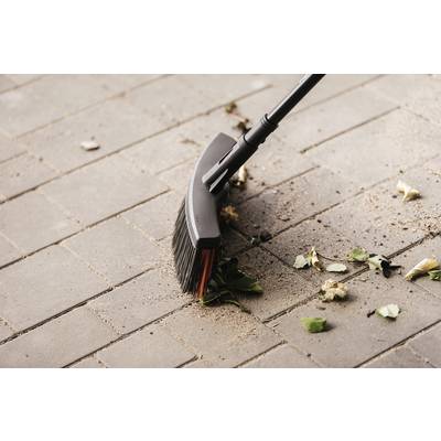 Un balai rassemble des feuilles sèches et des saletés sur un sol pavé.