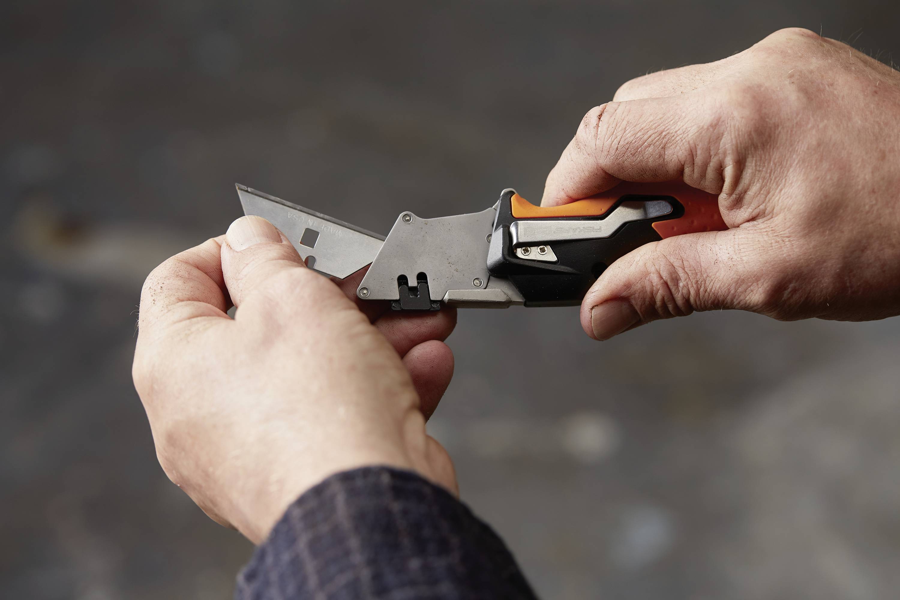 Une personne tient un cutter dans ses deux mains et fait sortir prudemment la lame. L'arrière-plan est flou.