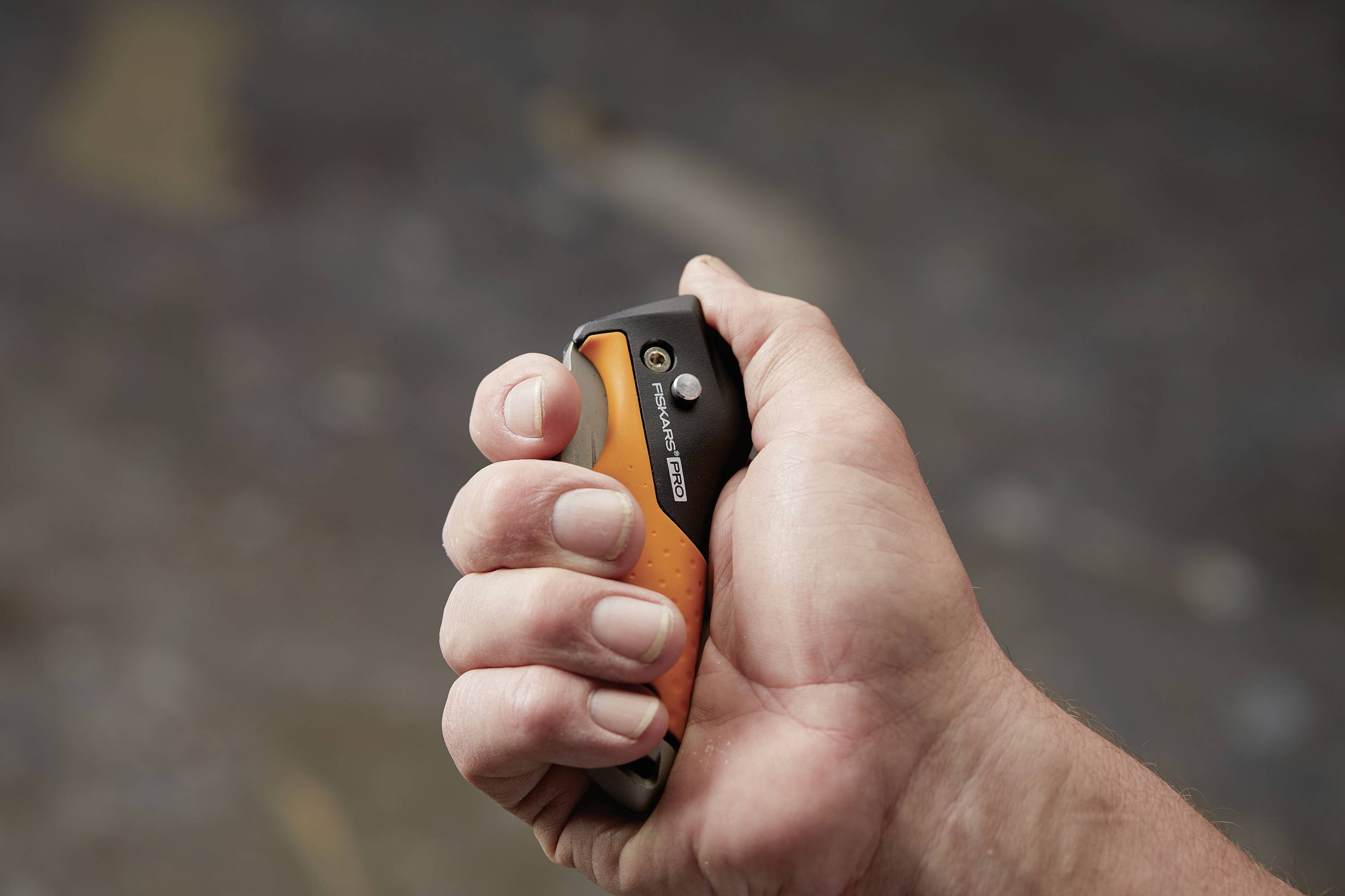 Une main tient un petit couteau de poche pliant avec une poignée noire et orange devant un arrière-plan flou.