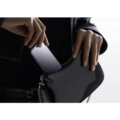 Une personne glisse un smartphone dans un sac à main noir, mettant en valeur le design élégant et la portabilité de l'appareil.