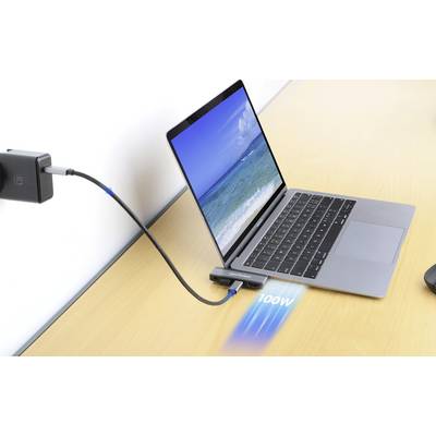 Un ordinateur portable sur une table est connecté via un câble à un adaptateur affichant 100W, avec une image de mer à l'écran.