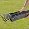 Une personne tient un appareil gris avec des dents noires ressemblant à un tube de télescope au-dessus d'une surface d'herbe verte.