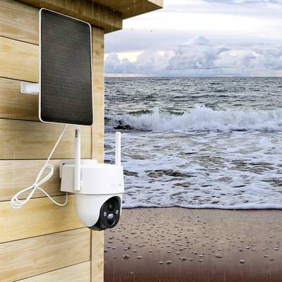 Caméra avec panneau solaire sur un mur en bois d'une maison, avec la mer et ses vagues en arrière-plan.