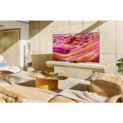Un salon moderne avec un grand téléviseur affichant une image abstraite et colorée. Des espaces de repos confortables et une table.