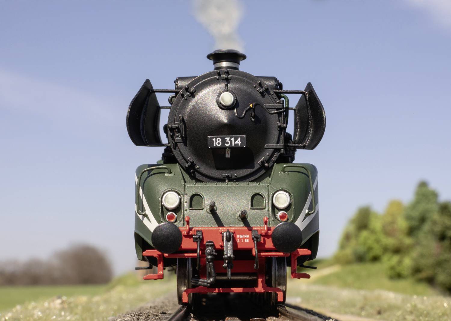 Locomotive à vapeur roulant sur des rails, photographiée de face, ciel bleu, arbres en arrière-plan. Locomotive portant le numéro '18 314'.