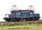 Un modèle bleu et blanc d'une locomotive électrique est posé sur une voie ferrée, entouré d'herbe. Deux pantographes rouges sont visibles.