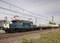 Un train miniature avec une locomotive bleue tirant plusieurs wagons-citernes sur un réseau ferroviaire miniature, entouré d'une installation industrielle.
