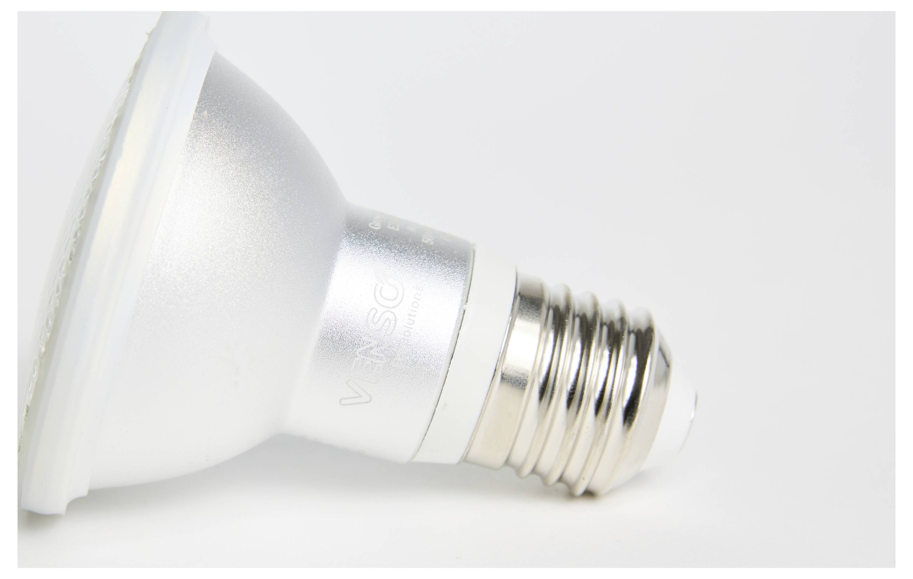 Une ampoule LED est posée sur le côté sur une surface blanche. Elle a un culot argenté et un socle à vis standardisé.